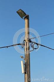 Concrete Utility Pole With Multiple Black Electrical Wires Small White Camera Cell Phone Tower Transmitter Metal Spikes White Camera Metal Spikes Reflectors