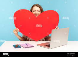 Online dating service. Beautiful woman holding big heart love symbol and  smiling, sitting at desk with laptop, advertising website for romantic date  Stock Photo - Alamy