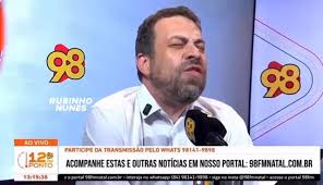 Ministro Guilherme Boulos com expressão irritada, gesticulando durante entrevista em estúdio de rádio.