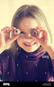 Smiling little girl holding two lychees in front of her eyes Stock Photo