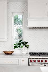 A White Wood Paneled Hood Is Mounted To White And Gray Chevron Backsplash Tiles Beside White Wood Paneling Farmhouse Kitchen Backsplash Chevron Tile Backsplash