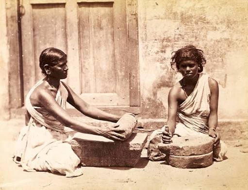 148 years old photo of two women with their kitchen appliances stone spice maker & grain grinding mill of Chennai in Tamil Nadu was taken in 1870 AD.