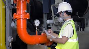 Industrial technician inspecting a gas pipe system, with safety equipment and monitoring tools visible, demonstrating routine maintenance practices.