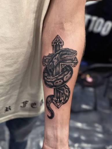Faith wrapped in power. ✝️🐍 Cross and serpent tattoo — a striking symbol of transformation, protection, and inner strength. Bold contrast, flowing movement, and timeless symbolism brought together in one custom design.