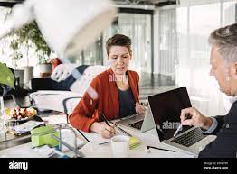 Geschäftsfrau beim Schreiben während des Gesprächs mit Kollegen  Stockfotografie - Alamy
