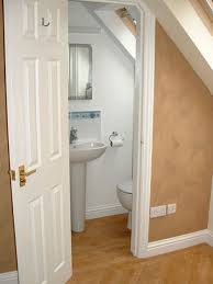 Attic bathroom with sloped ceiling and walls painted gray alongside a single washstand with white countertop which extends over the toilet atop gray hex under a sloped wood plank attic ceiling, this cottage style bathroom features a diamond shaped window is positioned above a black woven basket. Attic Bathrooms Google Search Attic Bathroom Plumbing Attic Bathroom Ideas Small Atti Small Attic Bathroom Attic Spaces Attic Bedroom Small