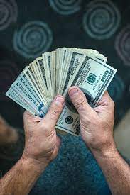 A businessman's hands counting hundred dollar bills at a table. Man Holding A Large Stack Of Fanned Out Hundred Dollar Bills By Carolyn Lagattuta