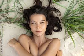 Foto Stock Nude beautiful woman on the nudist beach. Lady with nude perfect  body laying on sand. Gorgeous mixed race Caucasian Asian girl posing on  travel vacation holidays naked outdoors. Close-up portrait