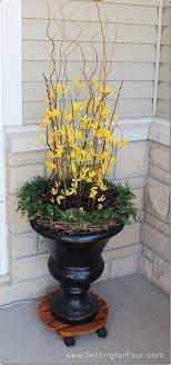 Urn With Faux Forsythia Curly Willow Branches Grapevine Wreath With Faux Boxwood Add A Spotlight In The C Front Porch Decorating Spring Decor Spring Planter