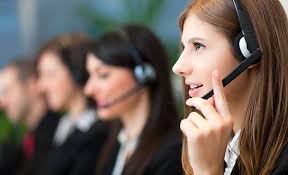 A woman interacts with a digital check-in kiosk that features a tablet screen displaying a user's profile image and a 'Confirm' button. She seems to be verifying her identity or checking in for an event or appointment. The setting suggests a modern office or reception area.