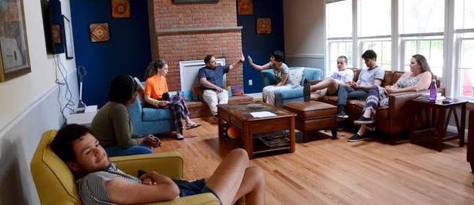 Group of people sitting in a shared living room during a community support discussion.