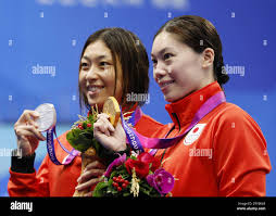 Reona Aoki (R) of Japan and compatriot Satomi Suzuki pose for photos after  winning gold and silver, respectively, in the women's 100-meter  breaststroke event at the Asian Games in Hangzhou, China, on