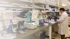Modern laboratory with bench equipment, microscope, centrifuge, and technologist in lab coat and mask