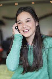 Stylish teen, beautiful young model girl with long blonde hair in black jeans and in fashionable red sweatshirt posing. Smiling Teenage Girl Talking On Mobile Phone Looking Black Hair Stock Photo 224392284