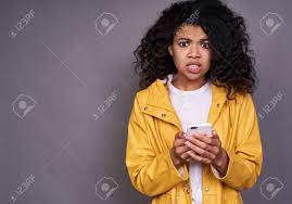 Well the hula hoop beats the shit. Surprised Not Understanding Young Cute Pretty African American Woman With Curly Puffy Hair In A Yellow Raincoat Holds A Smartphone In Her Hand Looks Straight Isolated On A Gray Background Stock Photo