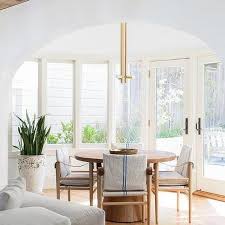 Transitional dining room features an oval blond wood dining table with black metal chairs on a blue and white rug layered on hardwood floors illuminated by six cone light chandelier. Baker Dining Chairs Design Ideas