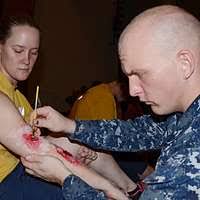 Hospital Corpsman 2nd Class David Haynesnorton, assigned to U.S. Naval  Hospital Guam, applies fake scars to Machinery Repairman 3rd Class Terri  Marcum, assigned to the submarine tender USS Frank Cable (AS 40),