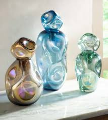 Gathering molten glass, adding colour, rolling it to shape, blowing to produce a hollow section. Dual Dented Iridescent Glass Vases Vivaterra
