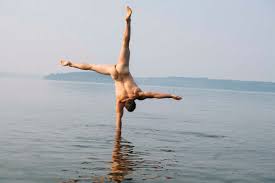 Rear view of nude man doing handstand in water stock photo