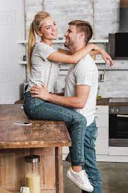 happy girlfriend sitting on kitchen counter and cuddling boyfriend 