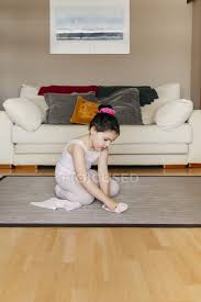 Portable or permanent resilient flooring for studio, stage, and touring. Side View Of Cute Girl In Leotard And Tights Sitting On Floor Near Sofa And Putting On Dance Shoes Before Ballet Rehearsal At Home Footwear Dancer Stock Photo 369803088