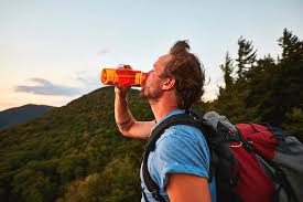 A traveler drinking bottled water while trekking in the mountains, emphasizing hydration.
