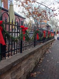 Black Wrought Iron Fence Decorated With Fresh Garland Lights Red Bows Located Christmas Decorations Diy Outdoor Outdoor Christmas Outdoor Christmas Lights