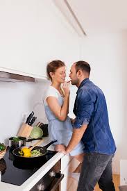 Age of persons on the photo: Free Photo Young Woman Sitting On Kitchen Counter Feeding Salad To Her Husband
