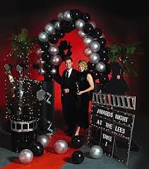 These hanging decorations feature a playful array of black, gold, and silver swirls, some with attached star clusters and silver and gold star cutouts. Hollywood Balloon Arch Shindigz Bottom Right Hand Corner Make Out Of Poster Boar Hollywood Party Theme Red Carpet Party Hollywood Theme Party Decorations