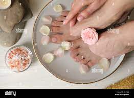 Mujer empapando sus pies en un tazón con agua, flores y pétalos en el suelo  de madera blanco, vista superior. Procedimiento de pedicura Fotografía de  stock - Alamy