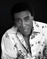 Portrait of comedian and variety performer Norman Vaughan playing the  guitar as his young son sings, circa 1962