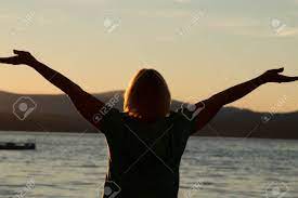 裏熟女、広げられた腕によって海と夕日に面したビーチに立っています。の写真素材・画像素材 Image 65488434
