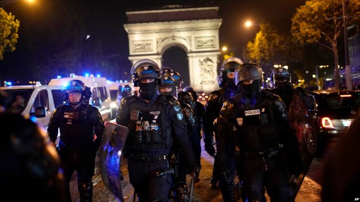 Fully geared riot police officers secure a perimeter near the Arc de Triomphe as authorities crack down on nationwide civil unrest., AI generated