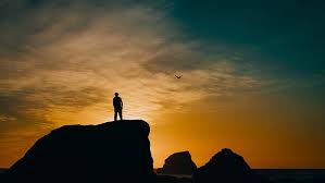 Silhouettes of a sad man with the background of the sunset sky. Hd Wallpaper Silhouette Of Man Standing On Rock Rocks Sunset Sea Bird Wallpaper Flare