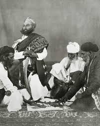 Rajput men playing the game of Puchesee - 1860s A print by Eugene Clutterbuck Impey in the early 1860s showing a group of men from Rajasthan in northern India playing pachisi. This