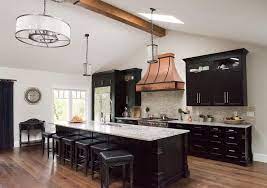 Light brown wood floor with a white farmhouse sink, shaker cabinets, black granite countertops, beige black mixed cement 6″x6″ backsplash, an island and black countertops. Black Kitchen Island With White And Gray Granite Countertops Transitional Kitchen