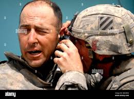 Sgt. 1st Class Ronald Sloan, a Lecanto, Fla., native, grimaces as Sgt. Paul  Brennan, a Wellingborough, England, native, examines his ear after an  explosion at Joint Security Station Sadr City in the