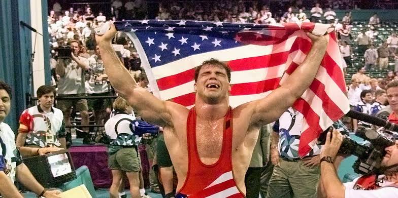 [Image: Kurt Angle celebrating Olympic gold medal win in 1996 with American flag]