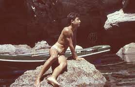 Nackter junger mann am strand auf einem stein