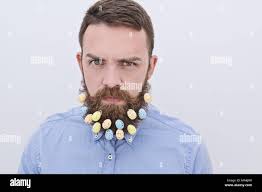 Charming bearded men looking at camera with Easter egg decoration in his  beard