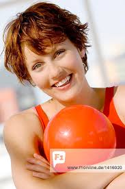 Junge lächelnde Frau auf einem großen rosa Ballon liegend