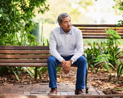 Image of person sitting on a bench in a park, looking thoughtful