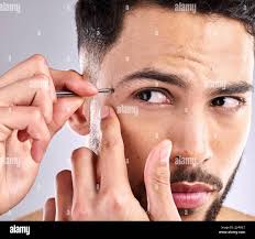 I dont like it when things are out of place. Closeup shot of a young man  plucking his eyebrows against a grey background Stock Photo