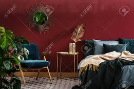 The only opulent pieces in the entire room are the desk and chair, which is upholstered in a rich red with detailed golden decorations. Gold Table Between Green Armchair And Bed In Sophisticated Red Bedroom Interior With Mirror Stock Photo Picture And Royalty Free Image Image 97566347