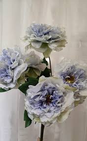 Sorridente fiorista bruna con fiori che prendono crisantemi dalla scrivania con rastrelliere sfocate sullo sfondo. Ricerca Prodotti Fiori Di Lena