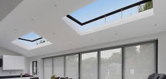 Skylights fitted to a vaulted ceiling accented with blond wood beams are positioned above an oak plank floor in a living room featuring a light gray sectional. Buying A Skylight Here S Everything You Need To Know