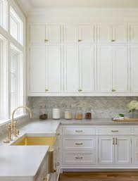 White Stacked Kitchen Cabinets Adorning Vintage Brass Latch Hardware Are Fixed Above A Marble Backsplash Lining Wh Home Kitchens Kitchen Remodel Modern Kitchen