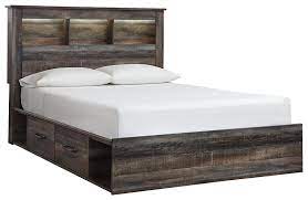 The pieces are a bed frame with a headboard, a nightstand, and a dresser or chest of drawers. Drystan Queen Bookcase Bed With 4 Storage Drawers B211b18 B10013 B21154 B21160 B21165 Complete Bed Sets Price Busters Furniture