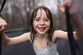 Contact your company to license this image. Smiling Girl Playing On A Trampoline In The Rain Untied States Toothy Smile Standing Stock Photo 472463504