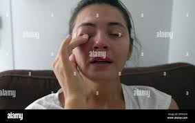 Traurige Frau, die tief einatmet und sich ängstlich fühlt. Weinende  weibliche Person nähert sich dem Gesicht mit verzweifeltem Ausdruck und  reibt das Auge während Hard tim mit der Hand Stockfotografie